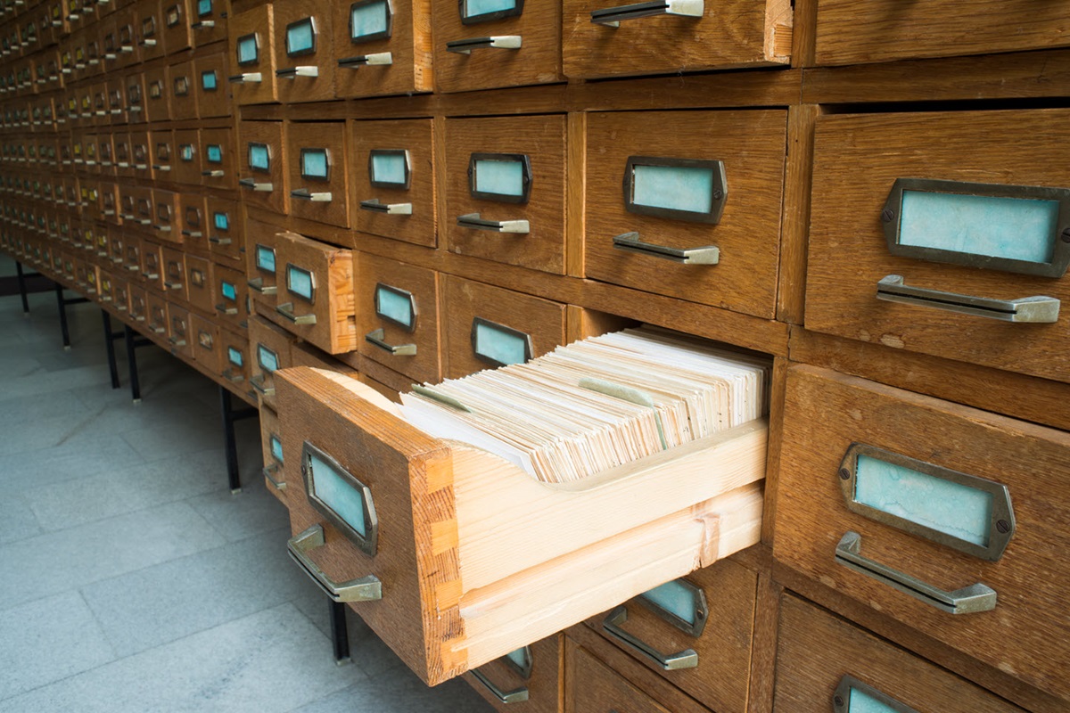 A wall of archive drawers extends across the frame. One shelf is pulled open to reveal it's full of file folders.