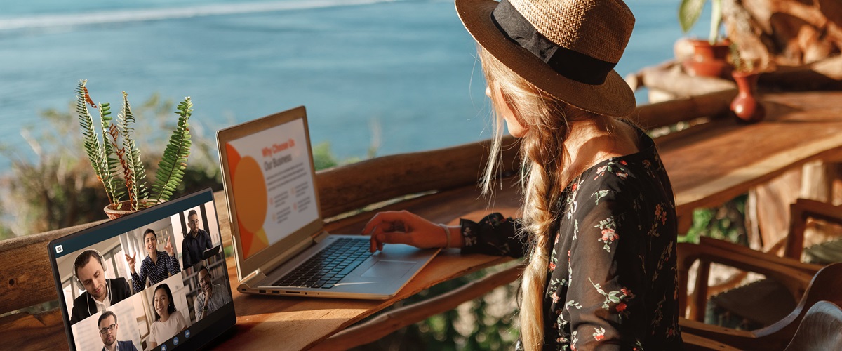 Seated woman working on a laptop with a portable monitor overlooking the ocean. 