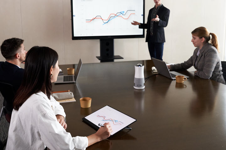 Meeting room of four business people around a table with a projector and the RICOH Portable Monitor being utilized. 